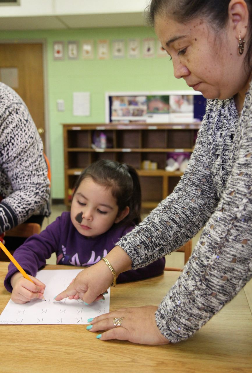 Kayla Ramirez practices writing the letter "k" with help from Evangelina Bravo. (photo/Johnny Bailey)