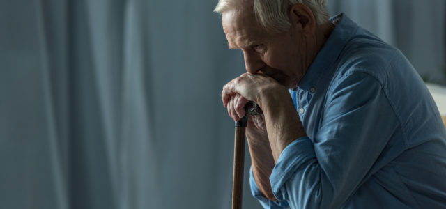 Senior sad man leans on a cane while sitting on sofa