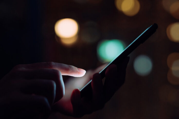 Close up of woman's hand using smartphone in the dark, against illuminated city light bokeh