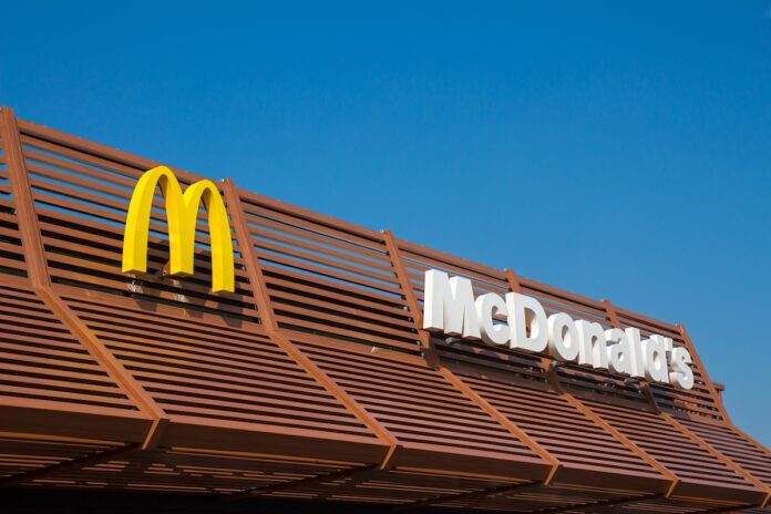 White McDonald's letters logo and yellow M logotype on a brown beam roof of the new McDonalds restaurant on a sunny blue sky day. Rotterdam the Netherlands. 1 March 2021.